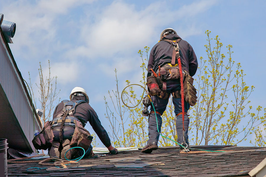 Two roofers perform roof repairs on a home